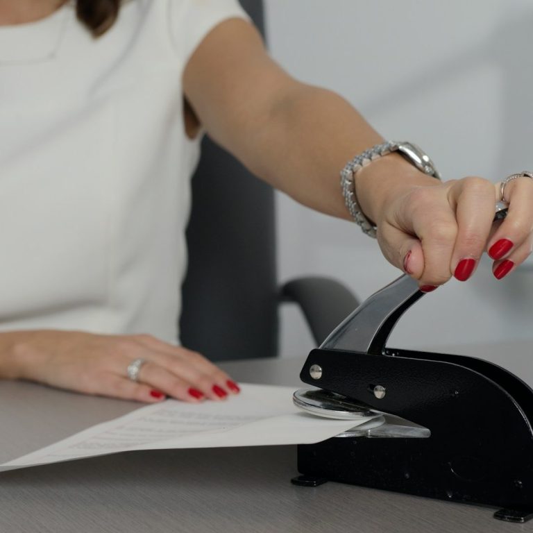 Stock photo of a person using a black notary seal A person using a black notary seal on a stack of paper on a desk.